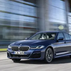 Granatowe BMW G30 540i sunie po drodze, odbijając się w nowoczesnej architekturze.