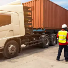 Ein Mann in Warnweste prüft Dokumente neben einem LKW mit Container. Alles bereit für den Frachttransportvertrag.