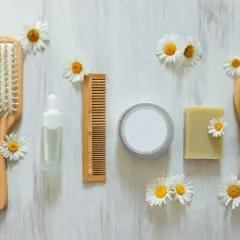 Cepillo, peine, jabón y serum de cuidado personal, todo cruelty free, rodeado de margaritas sobre fondo de madera.