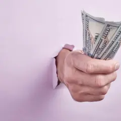 Dłoń przebija się przez różową ścianę, trzymając plik banknotów 100 USD. Ktoś walczy o zwrot kaucji.