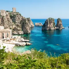 A picturesque bay with turquoise waters, rocky islets, and a historic tower, showcasing one of the most beautiful places in Sicily.
