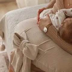 Mama karmi dziecko, układając je na poduszce do karmienia. Delikatny uścisk i spokój.
