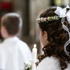 Dziewczynka z wiankiem i kokardą na głowie, trzymająca świecę. W tle chłopiec w białej komży. Biały tydzień po komunii.