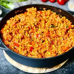 Herzhafter Djuvec Reis mit Mais und Paprika in einer Gusseisenpfanne, bereit zum Servieren.
