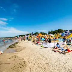 Słoneczna plaża w Ustce pełna ludzi, kolorowych namiotów i flag. Wiele atrakcji dla każdego.