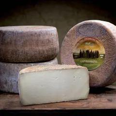 Formaggi di pecorino stagionato, uno intero con etichetta e uno tagliato a cuneo, su un tavolo di legno scuro.