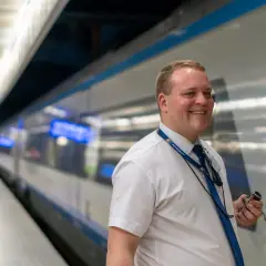 Uśmiechnięty mężczyzna w białej koszuli i granatowym krawacie, z identyfikatorem PKP Intercity, trzymający klucz. To jego pierwszy dzień po kursie na konduktora Intercity.