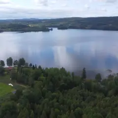 Spokojny finlandia krajobraz z jeziorem odbijającym chmury, otoczony lasami i zielonymi polami z kilkoma domkami.