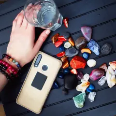 Ręka z bransoletkami trzyma szklankę wody, obok leżą kolorowe kamienie i telefon. Szukam odpowiedzi na pytanie: jaki jest mój kamień mocy.
