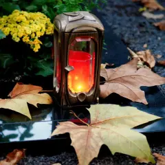 Grablicht auf einem Grabstein, umgeben von Herbstlaub und Blumen. Ein stiller Gruß zu Allerheiligen katholisch.