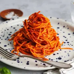 Ein Berg aus gekochte spaghetti braten mit Tomatensauce auf einem Teller mit blauen Tupfen. Eine Gabel liegt daneben.