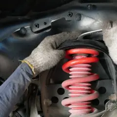 Mechanik w rękawiczkach dokonuje wymiany sprężyny amortyzatora w samochodzie.