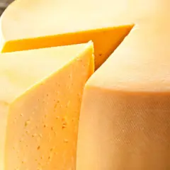 Kawałek sera Gouda z widocznymi oczkami i fragmentem całego kręgu sera.