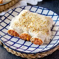Canelones de atún y huevo gratinados, cubiertos de bechamel y queso, servidos en plato a cuadros.