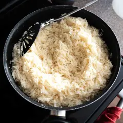 En stor kastrull med fluffigt, vitt ris står på spisen. En svart slev rör om i det nykokta riset, redo att serveras. Perfekt för en snabb middag, detta ris i kylen är en räddare i nöden.
