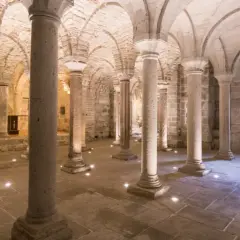 Cripta dell'Abbazia di San Salvatore, con colonne in pietra e volte a crociera illuminate da faretti a pavimento.
