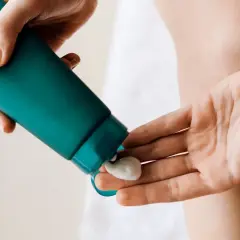 En hand klämmer ut en klick body lotion i ansiktet för återfuktning.