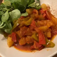 Un plat coloré de poivrons et pommes de terre mijotés, servi avec une salade verte. Une recette simple et savoureuse.