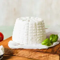 Świeża ricotta na desce, obok pomidorki i bazylia. Idealny składnik do lekkich dań.
