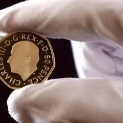 Złoty suweren moneta z wizerunkiem Karola III, trzymana w białej rękawiczce.
