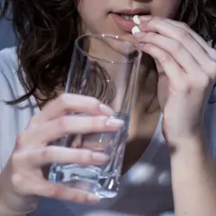 Kobieta bierze tabletki mianseryny, trzymając szklankę wody.