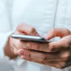 Dłonie trzymające smartfon, uważaj na oszustwa typu smishing, które mogą przyjść w każdej chwili.