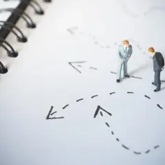 Figurki biznesmenów analizują ścieżki na mapie, symbolizujące bariery wejścia na rynek i strategie ich pokonywania.