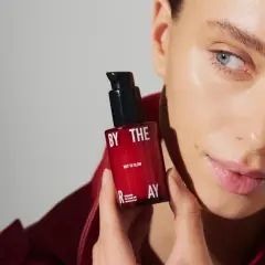 Kobieta z serum z peptydami w kosmetyce. Czerwona buteleczka z napisem "WAY TO GLOW" i "multipeptide face serum".