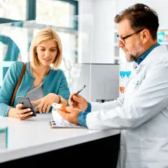 Farmacista spiega a cliente un esempio di farmaci off-label, mostrando una scatola e consultando il telefono.