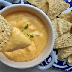 Chrupiące nachos zanurzane w kremowym sosie z serka topionego, ozdobionym gałązką ziół. Idealna przekąska!