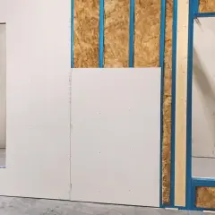 Fase iniziale di come fare una parete in cartongesso: pannelli bianchi fissati su struttura metallica blu, con isolamento visibile.