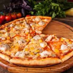 Pyszna pizza z kurczakiem i kukurydzą, podana na drewnianej desce. Obok świeże pomidorki i zioła.