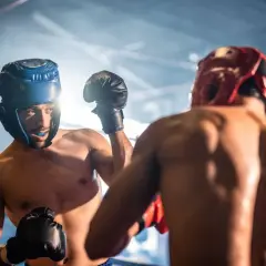 Two boxers in a ring, wearing headgear and gloves, engage in sparring. The intense training session highlights their focus and determination.