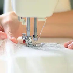 Dłonie szyjące białą, delikatną tkaninę na maszynie do szycia.