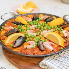 En stor paella med räkor, musslor, gröna ärtor och citronklyftor. Perfekt för ett somrigt paella recept.