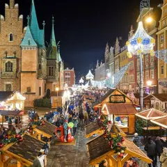 Tłoczny, rozświetlony jarmark bożonarodzeniowy, największy jarmark bożonarodzeniowy w Polsce, z kramami i ludźmi w nocnej scenerii.