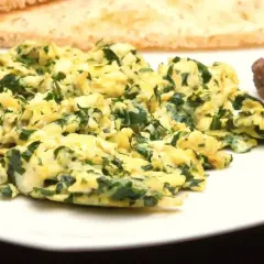 Pyszna jajecznica ze szpinakiem na talerzu, obok grzanki i fasolka.