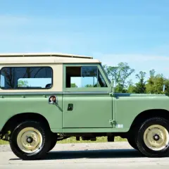 Land Rover Santana verde y crema, listo para una aventura todoterreno junto a un lago.