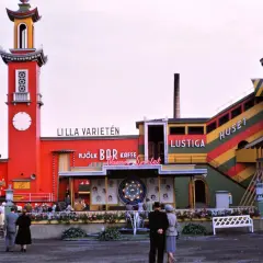 Färgglatt lustiga huset med torn och rutschkana. Folk minglar vid bar och kaffe.