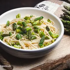 Spargel Pasta: Ein Teller Spaghetti mit frischem, grünem Spargel, daneben ein Bund Spargel.