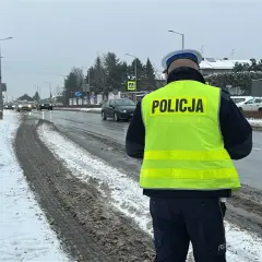 Policjant w kamizelce odblaskowej stoi przy drodze, gdzie kiedy zabierają prawko za prędkość. Śnieg i błoto na poboczu.