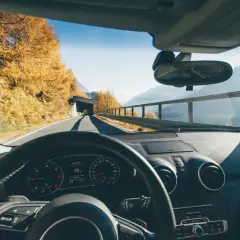 Volant d'une voiture en mouvement, tableau de bord affichant 16 km/h. Paysage d'automne en Italie, arbres dorés, montagnes et tunnel.