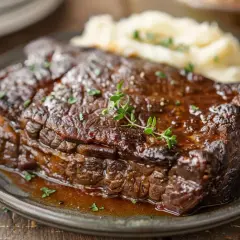 Un plat de boeuf braisé, tendre et juteux, servi avec une purée de pommes de terre crémeuse et garni de thym frais.