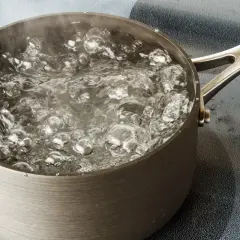 Une casserole en métal sur une plaque de cuisson, l'eau est en train de bouillir avec des bulles et de la vapeur.