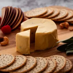Un delizioso formaggio vegano, con lamponi, mele, frutta secca e cracker su un tagliere di legno.