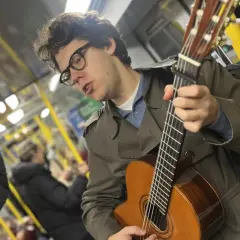 En ung man med glasögon spelar gitarr på tunnelbanan, en musikalisk själ med stockholm roots.