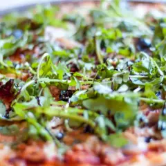 Pyszna pizza z tuńczykiem, rukolą i oliwkami, polana sosem balsamicznym. Idealna na szybki obiad.