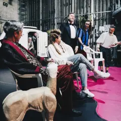 Poskromienie złośnicy obsada: aktorzy w teatralnych strojach, siedzą i stoją na scenie, obok biały rekwizyt.
