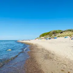 Sonniger Tag am Strand Nonnevitz. Menschen entspannen sich unter bunten Schirmen, während sanfte Wellen das Ufer erreichen.