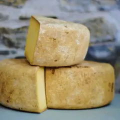 Formaggio di fossa stagionato, con crosta rustica e pasta gialla, impilato su uno sfondo di pietra grezza.